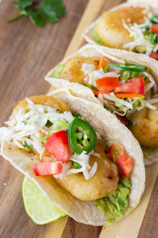 Fried shrimp tacos topped with slaw and jalapenos on a wood board.