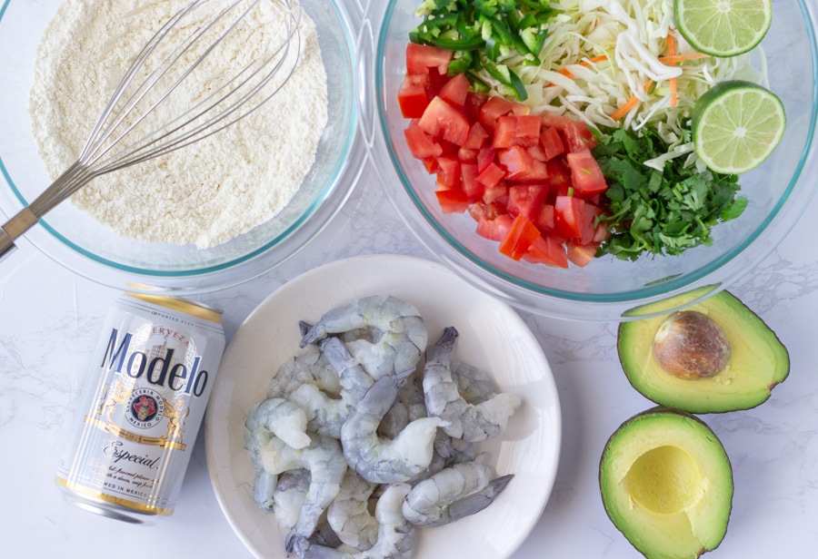 Bowl of flour, a plate of raw shrimp, beer can, and bowl of slaw.