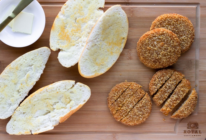 Buttered Rolls and cooked chik patties on a wood cutting board.