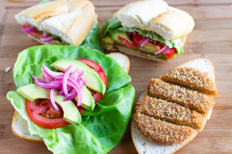 2 tortas with toppings on one bun and sliced chik patty on the other side and one sliced sandwhich in the back.