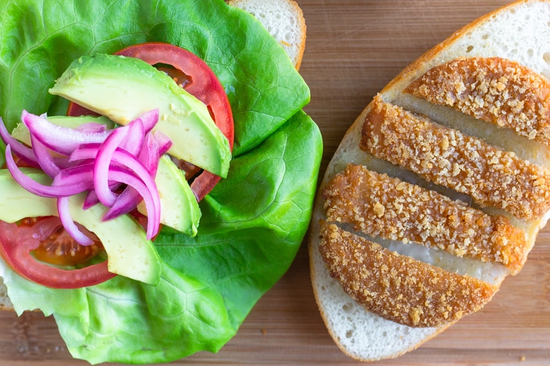 Overhead image of torta with toppings on one bun and sliced chik patty on the other side.