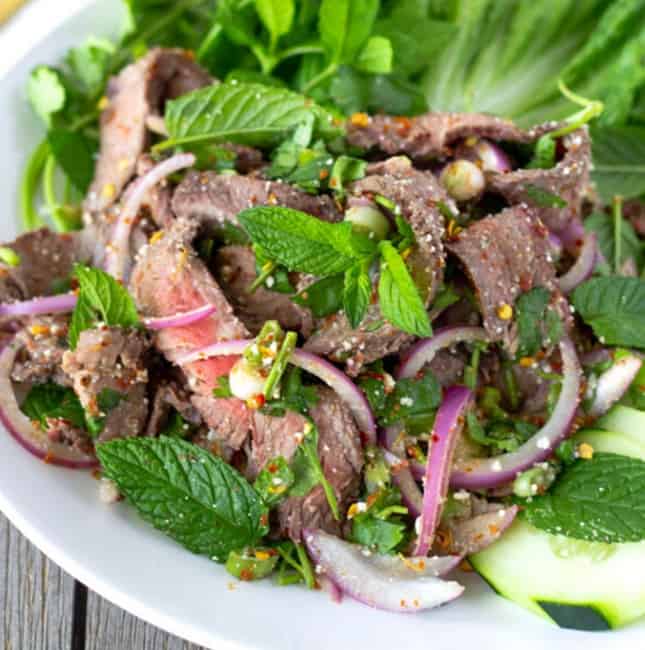 Up close view of sliced steak salad with mint, red onions, and a spicy Thai dressing.