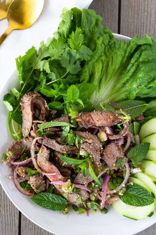 Overhead view of Beef Salad on a white plate garnished with lettuce, cucumbers, cilantro, and mint.