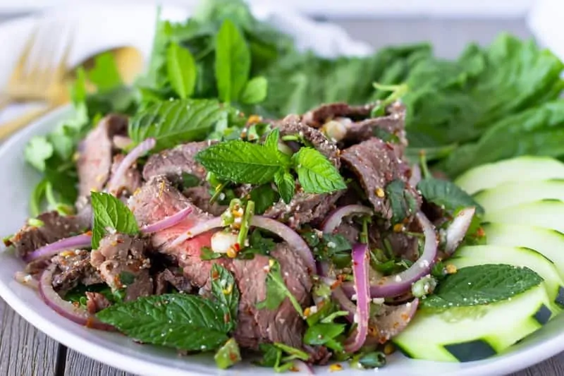 Tiro en ángulo ancho de ensalada de carne tailandesa en un plato blanco.