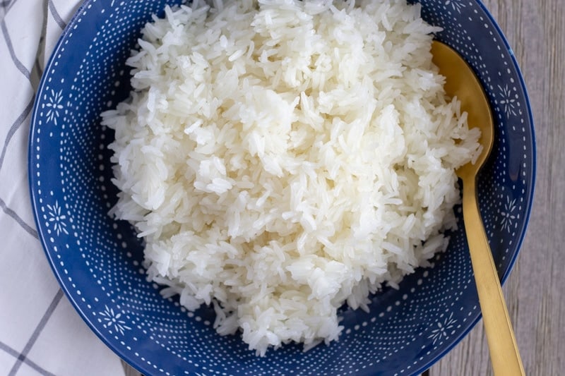 Blue bowl filled with cooked Thai sticky rice and a gold spoon.