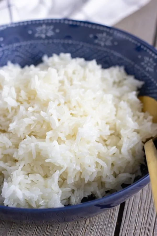 Blue bowl filled with cooked Thai sticky rice and a gold spoon.