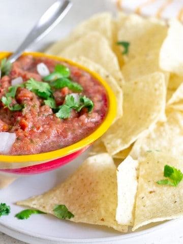 Yellow bowl holding tomato salsa on a plate with tortilla chips.