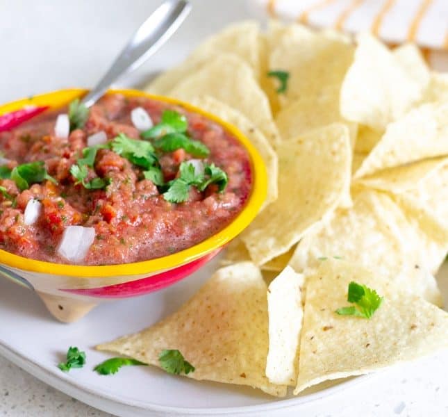 Yellow bowl holding tomato salsa on a plate with tortilla chips.