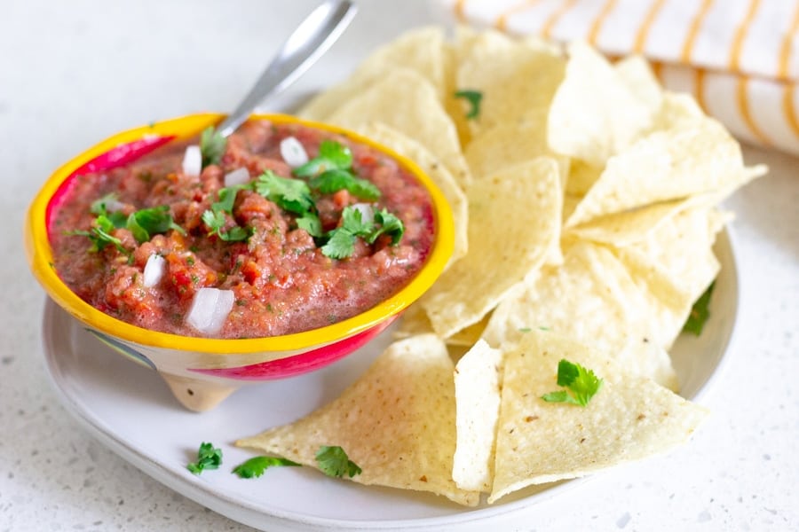 Yellow bowl holding tomato salsa on a plate with tortilla chips.