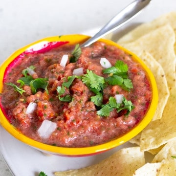 Yellow bowl holding salsa on a plate with tortilla chips.