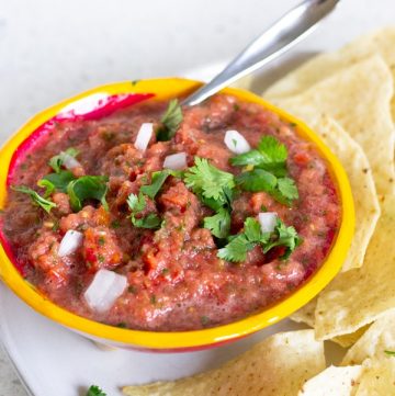 Yellow bowl holding salsa on a plate with tortilla chips.