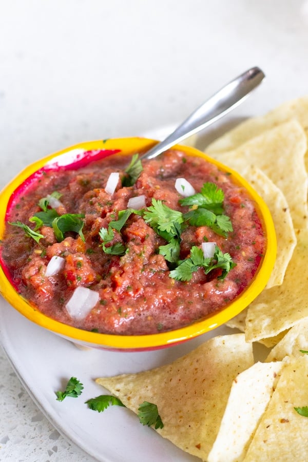 Yellow bowl holding salsa on a plate with tortilla chips.