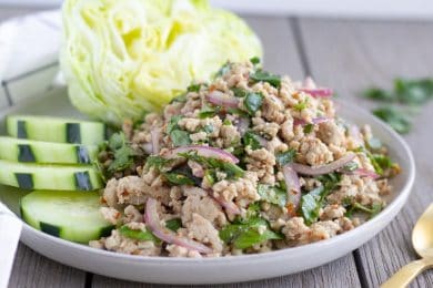 Horizontal view of finished Larb Gai on a plate with lettuce and cucumbers.