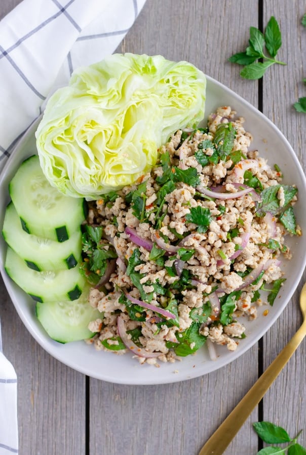 Overhead view of finished laap Gai on a plate with lettuce and cucumbers.