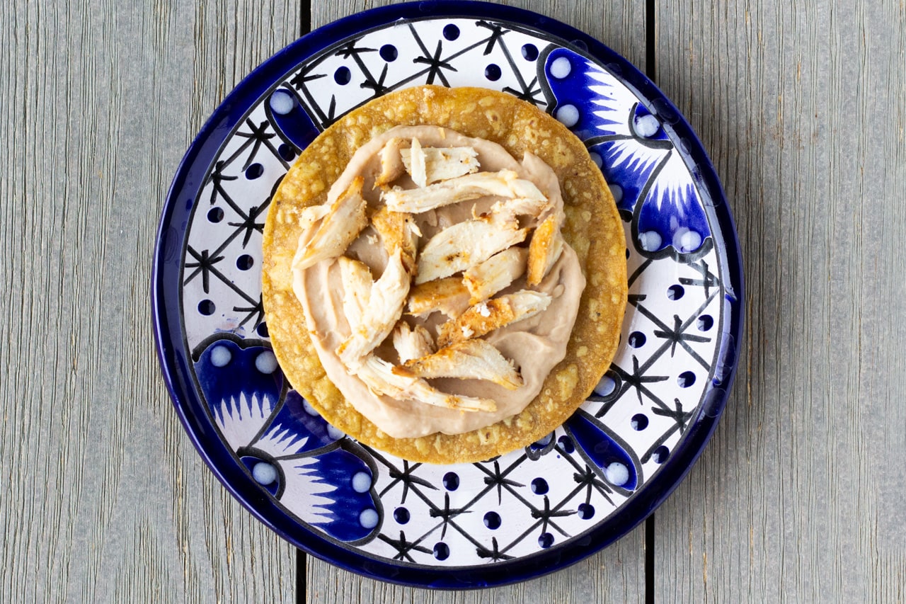 Tostada shell with a layer of refried beans and shredded chicken