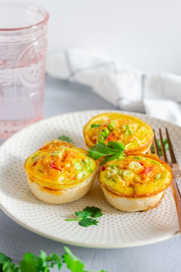 Three Sausage Egg quiche cups on a plate with a fork on the side and garnished with cilantro.