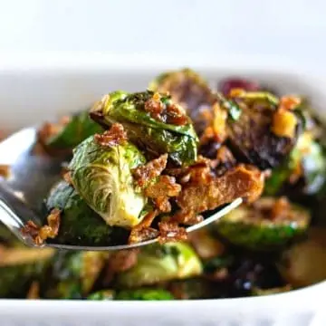 Spoon holding roasted Brussel sprouts with crispy onions.