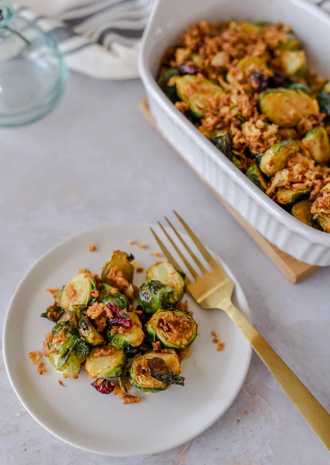 Maple and cranberry brussels sprouts in a white dish and some on a small plate.