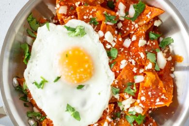 Overhead view of chilaquiles in a skillet with cilantro on the side and a pink glass of water.