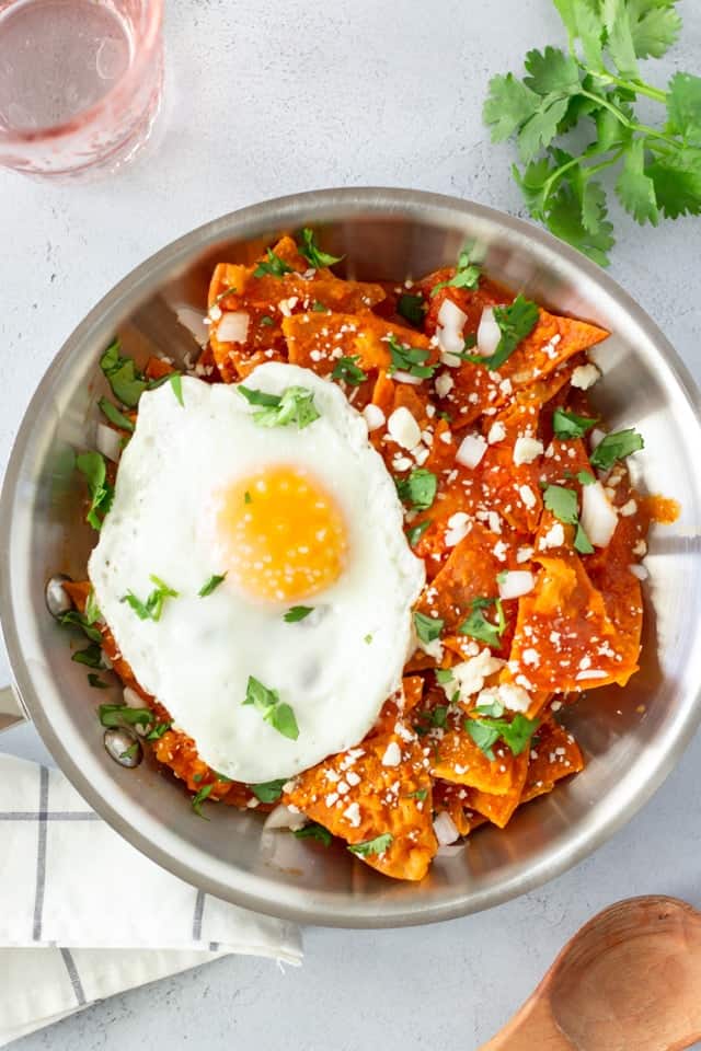 Overhead view of chilaquiles in a skillet with cilantro on the side and a pink glass of water.