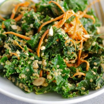 Kale salad topped with carrots and peanuts in a white bowl.