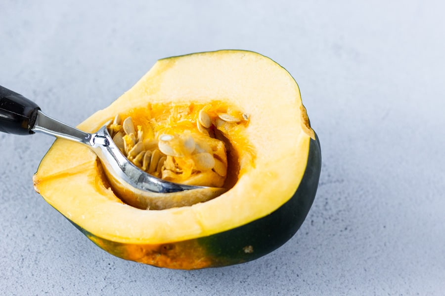 An ice cream scoop being used to scoop out the seeds inside the acorn squash.