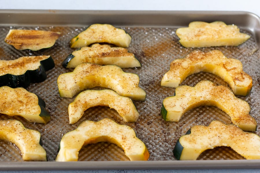 Acorn squash on a baking sheet with spices and oil.