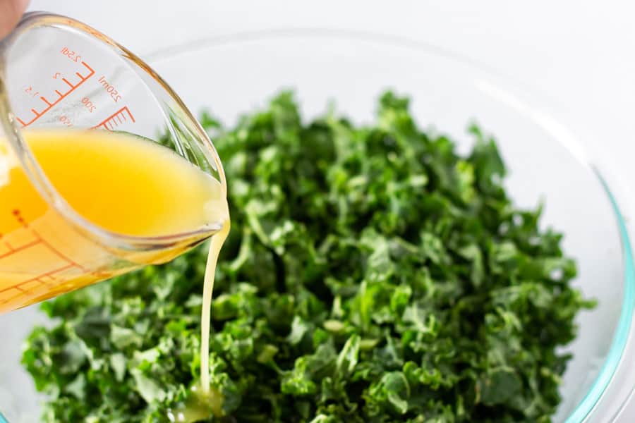 Dressing in a measuring cup being poured into kale leaves.
