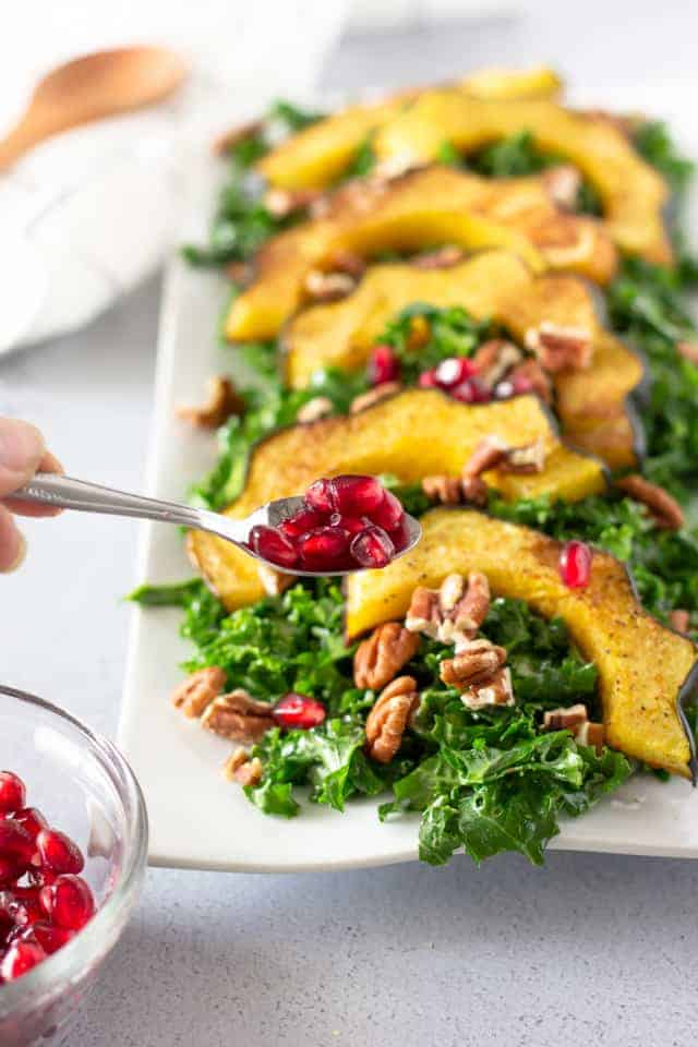 Spoon holding pomegranate seeds over salad.