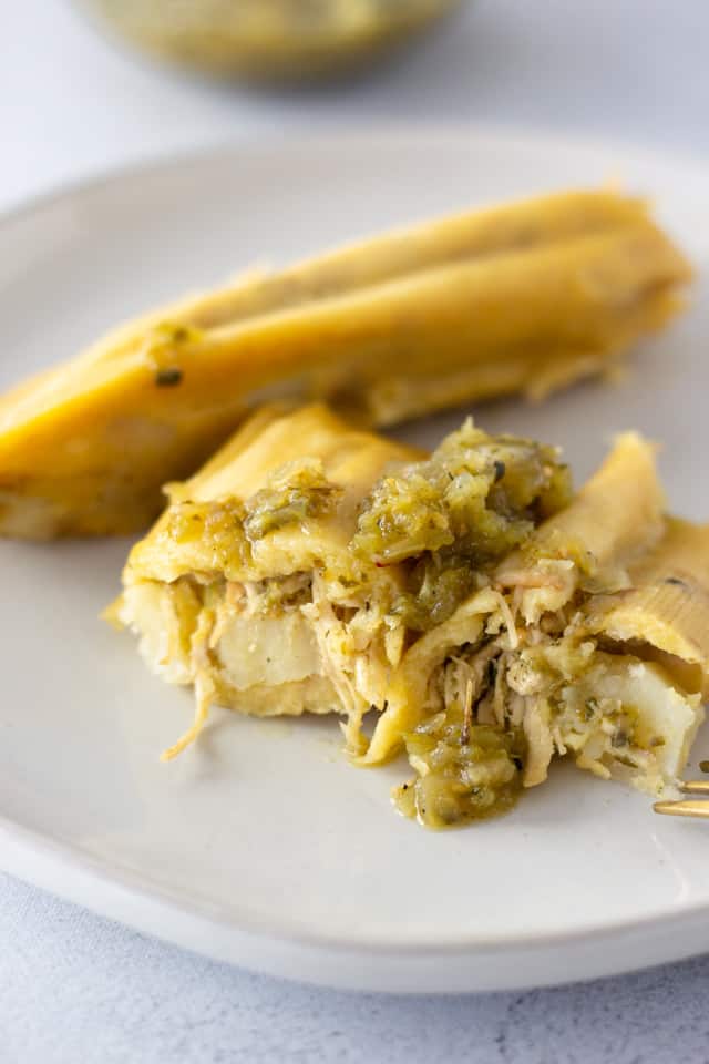 Two tamales on a plate with one cut in half to see filling.