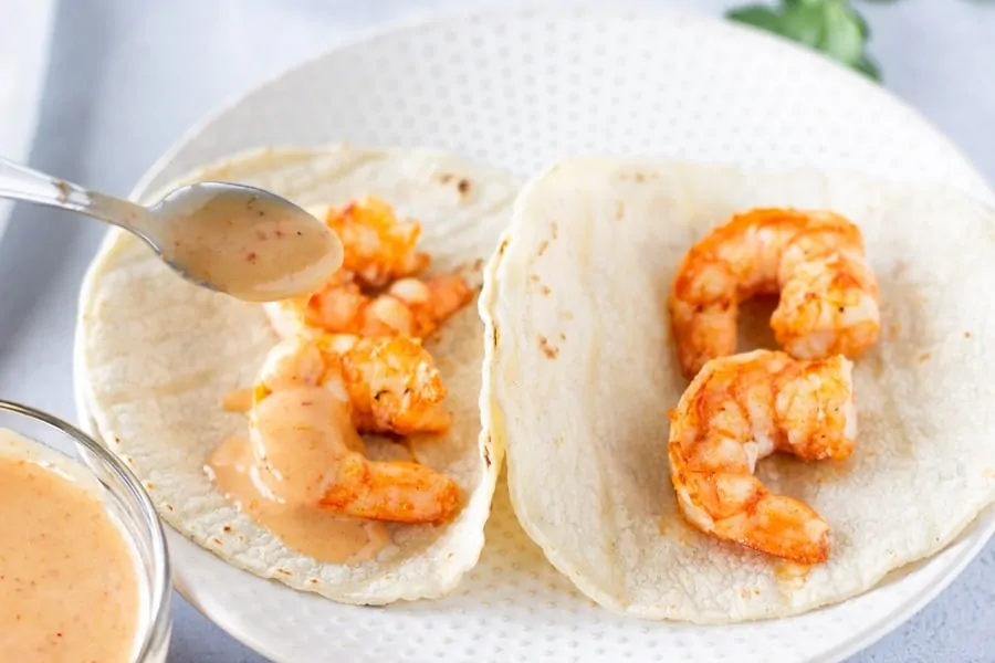 Two Pieces of shrimp on tortillas with red curry sauce being drizzled on top.