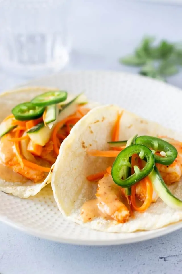 Two Tacos on a plate with a glass of water in the background.