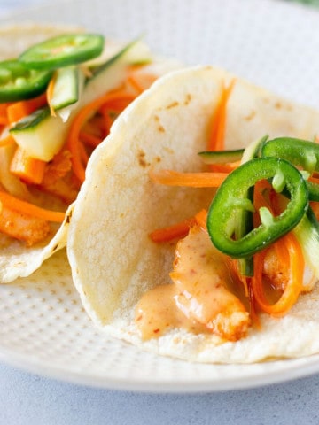 Two shrimp tacos topped with carrots, cucumber, and jalapeno slices.
