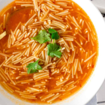 Noodles in a tomato based broth and garnished with cilantro.
