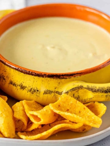 Feature image of queso in a yellow bowl with chips on the side.