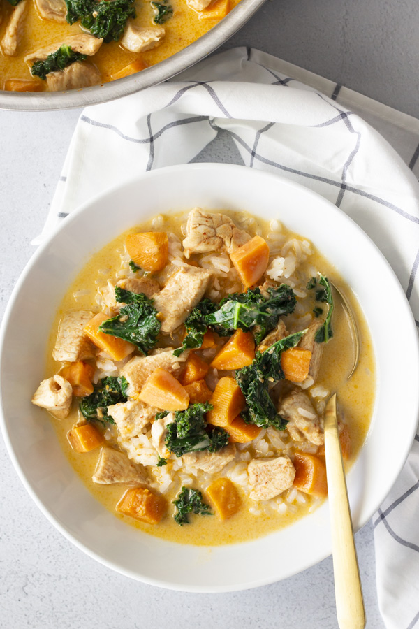 Overhead view of curry in a white bowl and a napkin on the side.