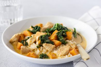 Curry in a white bowl with a gold spoon and glass in the background.