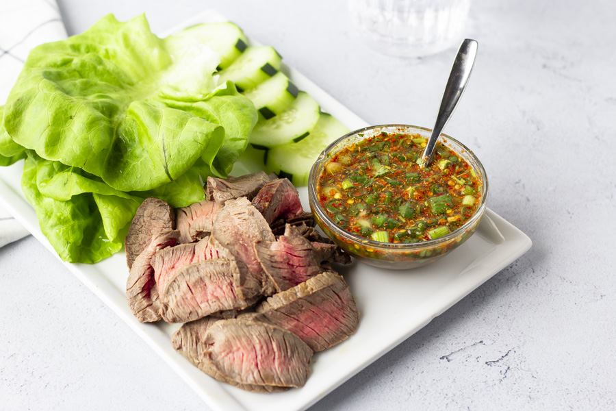 Finished plate of Crying Tiger- sliced steak, lettuce leaves, sliced cucumbers, and dipping sauce.