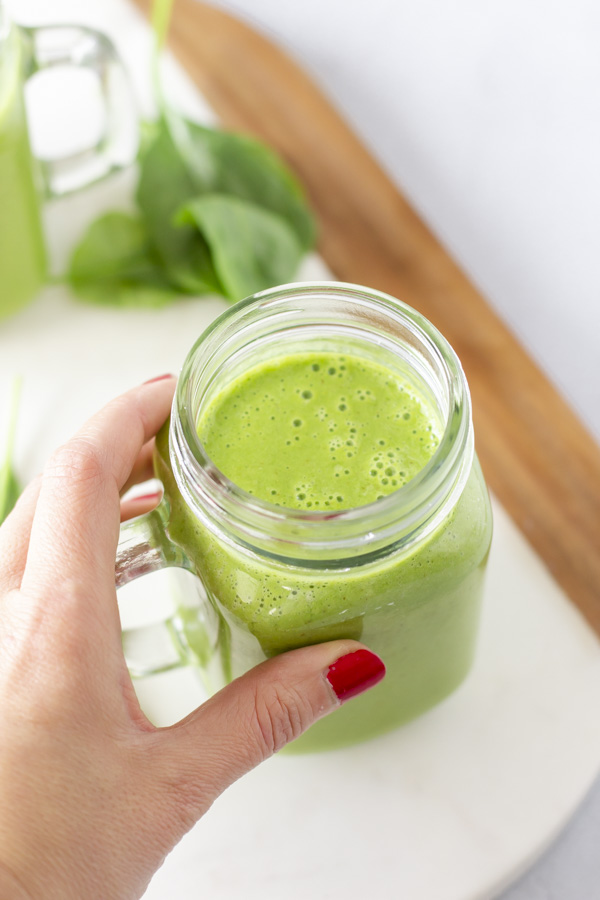 Hand holding a green smoothie.