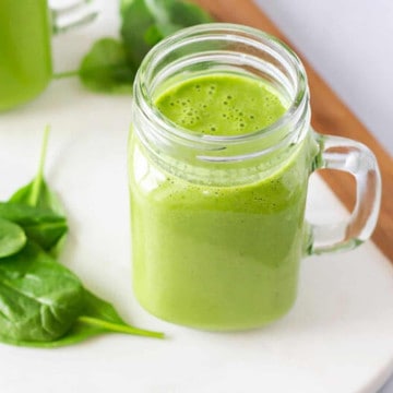 Up close view of green smoothie in a glass cup with spinach on the side.