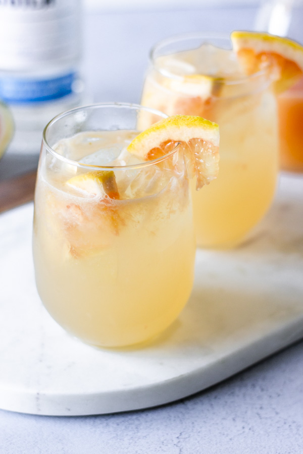 Two stemless wine glasses with paloma cocktail and garnished with slices of grapefruit.