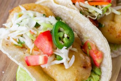 Shrimp tacos on a brown cutting board.
