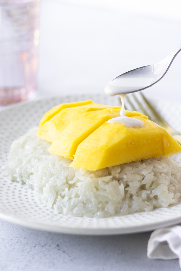 Spoon with coconut milk pouring over mango pieces.