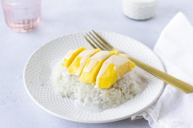 Sweet rice on a plate topped with mango and coconut milk, gold fork on the side.