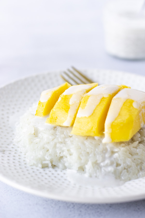 Sweet rice on a plate topped with mango and coconut milk.