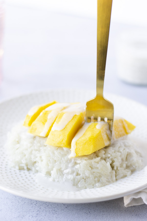 Gold fork piercing a mango on top of rice.