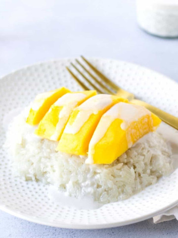 Plate with a mound of rice topped with sliced yellow mango and coconut sauce.