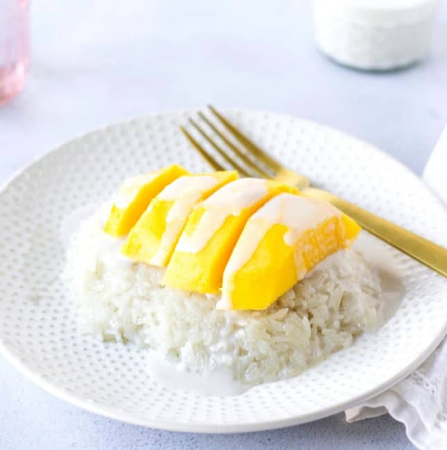 Plate with a mound of rice topped with sliced yellow mango and coconut sauce.