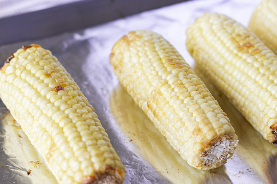 Roasted ears of corn on a foil lined baking sheet.