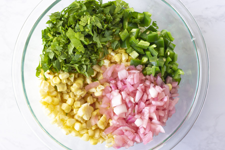 Ingredients for corn salsa in a bowl. Corn, red onion, jalapenos, and cilantro.